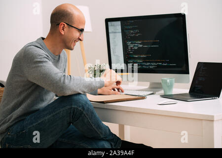 Programmatore, lavorando dietro la scrivania, analizzando il codice sullo schermo nero. Foto Stock