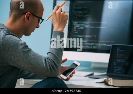 Programmatore, lavorando dietro la scrivania, analizzando il codice sullo schermo nero. Foto Stock