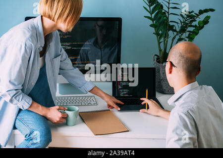 Programmatore, lavorando dietro la scrivania, analizzando il codice durante una sessione di chat con un collega Foto Stock