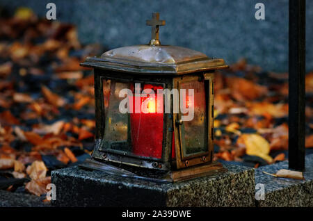 Vecchio danneggiato luce gravi fatti di metallo con la masterizzazione di candela su una tomba con foglie di autunno in sfondo sfocato Foto Stock