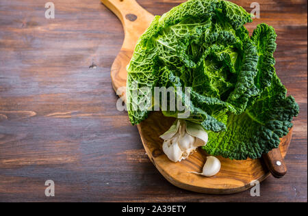 Crudo fresco cavolo verza con aglio e il coltello su sfondo di legno Foto Stock