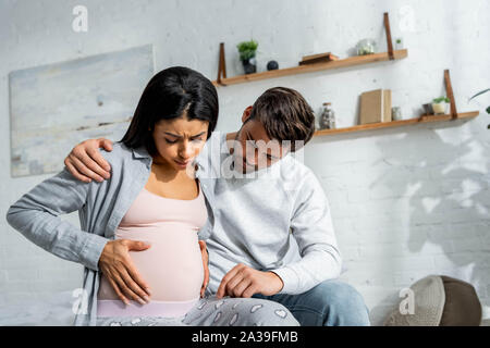 Uomo bello abbracciando africana incinta donna americana in pigiama Foto Stock