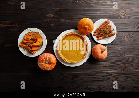 Vista dall'alto di tutta la varietà di zucche, torta di zucca cotta tutta la carota e fette di zucca sul buio superficie in legno Foto Stock