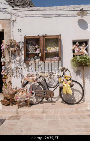 Un display di bambole di pezza e una vecchia bicicletta al di fuori di un negozio di souvenir in una tradizionale casa Trullo in Alberobello, Puglia, Italia. Foto Stock