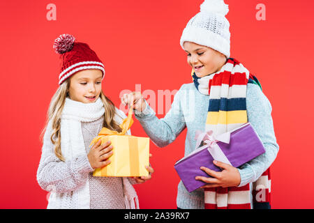 Due ragazzi sorridenti in inverno abiti azienda presenta isolato su rosso Foto Stock