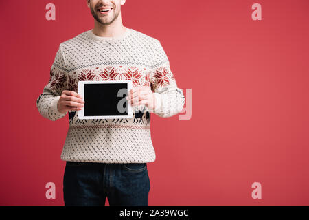 Vista ritagliata dell uomo in inverno maglione mostra tavoletta digitale con schermo vuoto, isolato su rosso Foto Stock