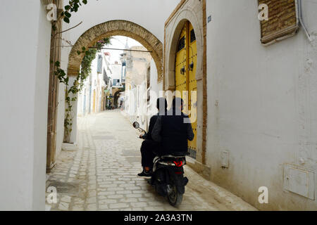 Due giovani uomini tunisini in sella a una moto attraverso le strade pedonali del quartiere Hafsia della Medina (città vecchia) di Tunisi, Tunisia. Foto Stock