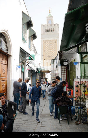 La gente in un vicoletto pedonale nel cuore della medina (città vecchia) di Tunisi con il quadrato minareto della moschea Zeitoun visto in background, Tunisia. Foto Stock