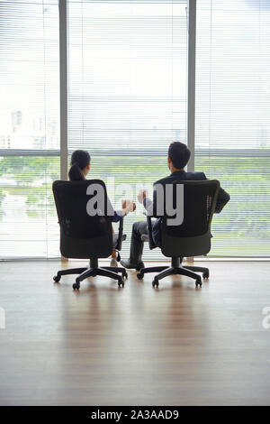 Azienda giovane seduto in un moderno ufficio vuoto a bere caffè e godendo cityscape, vista dal retro Foto Stock