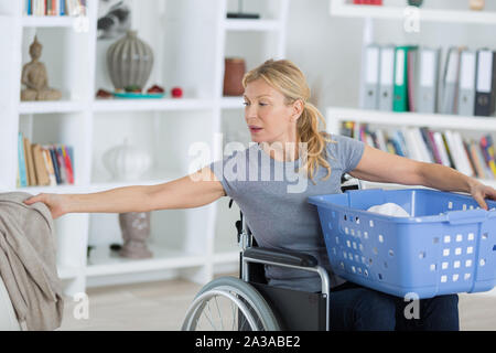 La donna in sedia a rotelle cestello di contenimento e di presa di servizio lavanderia Foto Stock