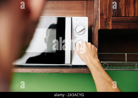 Uomo che utilizza un forno a microonde per riscaldare il cibo per la cena, vista dal retro Foto Stock