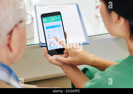 L'infermiera che mostra senior paziente come tenere il diario alimentare tramite applicazione mobile Foto Stock