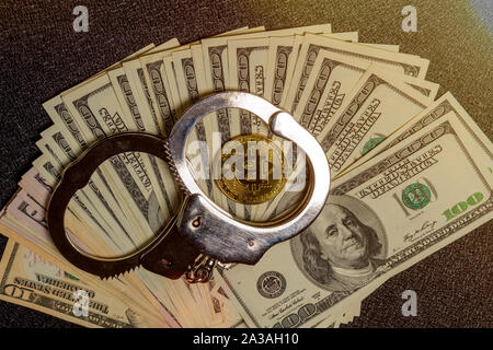 In manette su centinaia di fatture del dollaro e oro una moneta bitcoin. Vista superiore Foto Stock