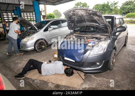 Mechanic sdraiato e lavorando in auto presso il garage. I meccanici che lavorano in auto service. Auto riparazione e manutenzione. Foto Stock