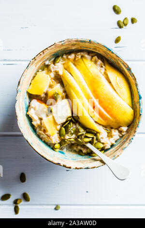 Farina di avena con pera e i semi di zucca in una ciotola di ceramica su un bianco sullo sfondo di legno. Foto Stock