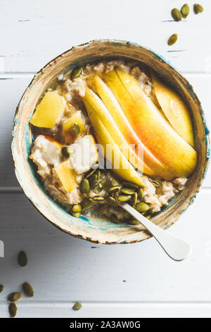 Farina di avena con pera e i semi di zucca in una ciotola di ceramica su un bianco sullo sfondo di legno. Foto Stock