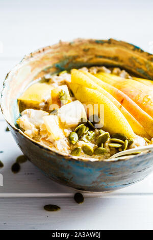 Farina di avena con pera e i semi di zucca in una ciotola di ceramica su un bianco sullo sfondo di legno. Foto Stock