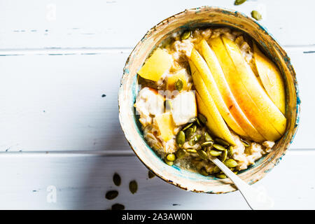 Farina di avena con pera e i semi di zucca in una ciotola di ceramica su un bianco sullo sfondo di legno. Foto Stock