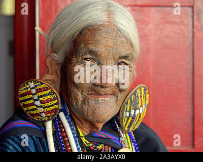 Vecchio mento Kaang hill-tribe donna con linea tradizionale tatuaggi facciali e di elaborare i tribali orecchini pone per la telecamera (colpo di testa). Foto Stock