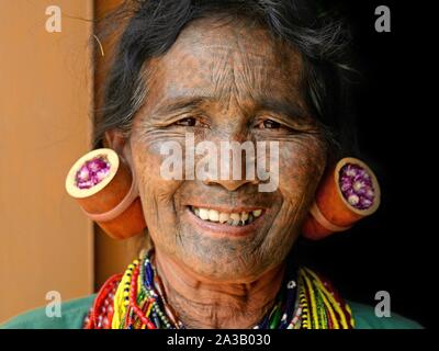 Vecchio mento Kaang donna tribale con tratteggiata tatuaggi facciali e tradizionali tappi di lobo nel suo orecchioni allungato sorrisi per la fotocamera. Foto Stock
