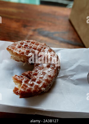 Fresche, vetrate parzialmente mangiato ciambella di apple seduti su un tavolo di legno in un locale negozio donut. Foto Stock