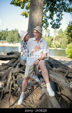 Amorevole moglie abbracciando il marito mentre è seduto vicino a tree Foto Stock