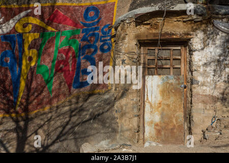 Ombre di un albero sulla colorata Buddista Tibetana script dal lato di una porta chiusa a chiave per una meditazione grotta presso il monastero di Drepung vicino a Lhasa, in Tibet. Foto Stock