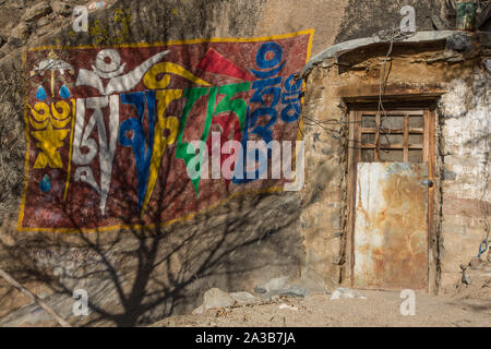 Ombre di un albero sulla colorata Buddista Tibetana script dal lato di una porta chiusa a chiave per una meditazione grotta presso il monastero di Drepung vicino a Lhasa, in Tibet. Foto Stock