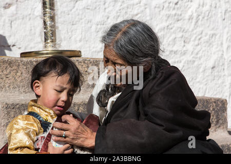 Una nonna Khamba dal Kham regione del Tibet aiuta a suo nipote durante un buddista religioso pellegrinaggio del Potala a Lhasa, in Tibet. Foto Stock