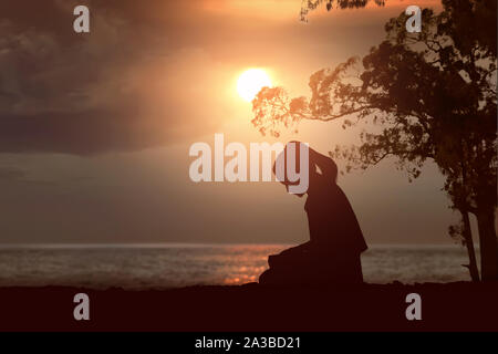 Silhouette di donna leggere la Bibbia sulla spiaggia con un Cielo di tramonto sullo sfondo Foto Stock