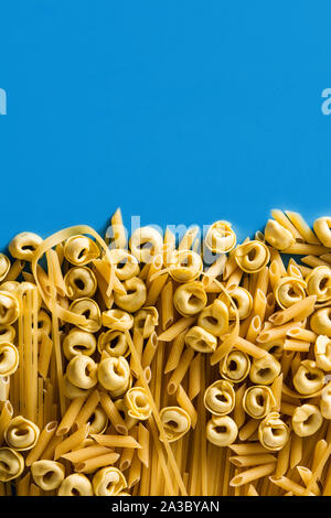 Diversi tipi di pasta. Ravioli, pasta di penne tortellini e capellini su sfondo blu Foto Stock