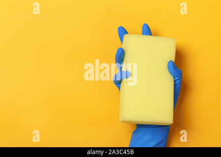Una mano in una protezione di guanto blu contiene una spugna su un giallo sfondo colorato. Foto Stock