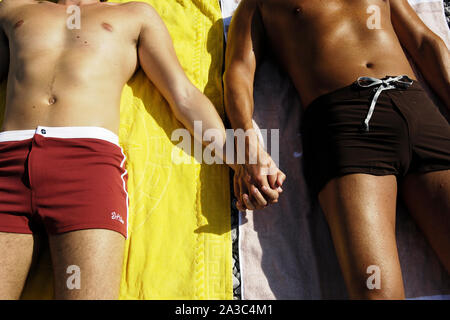 Due uomini che giace sulla spiaggia mano nella mano Foto Stock