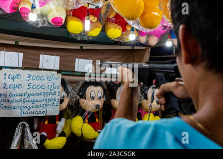 Un uomo asiatico sta puntando un fucile ad aria compressa che gli incendi pellet a una carta bersaglio mentre cercando di vincere un peluche ad una fiera in Kampong Cham, Cambogia. Foto Stock