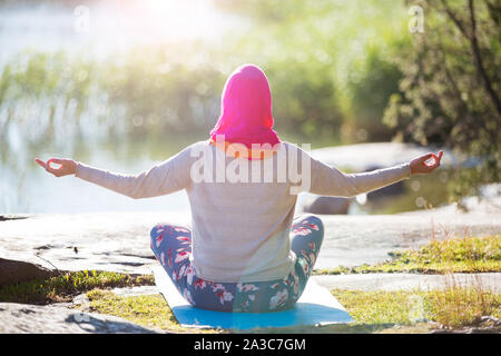 Donna attraente in hijab formazione nel parco, meditando. Facendo esercizi yoga su aria fresca e godendo di mattina presto. Uno stile di vita sano Foto Stock