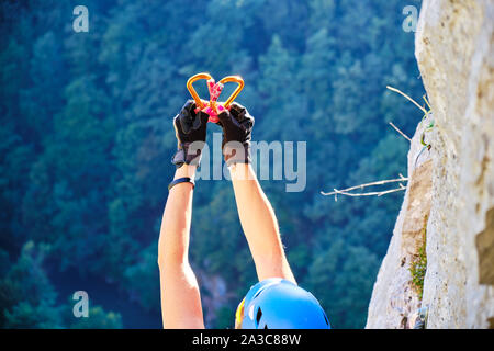 Cuore fatta di due moschettoni brilla al sole, sorretto da una donna scalatore sulla via ferrata in Peretele Zanelor, Vadu Crisului, Romania, su un Foto Stock