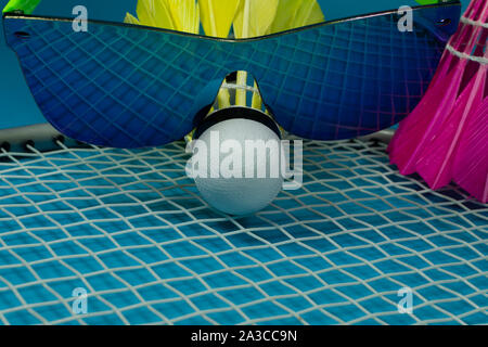 Selvaggina di penna colorati badminton volano con occhiali da sole in appoggio su una racchetta su uno sfondo blu in una chiusura ancora vita Foto Stock