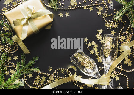 Lussuoso golden confezione regalo con due bicchiere di champagne risplendere su sfondo nero. Festa di Natale. Lay piatto. Vista da sopra. Xmas pattern. Foto Stock