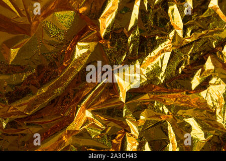 Creative dello sfondo della foto di oro accartocciata olografico lamina con orange punti di luce e ombre Foto Stock