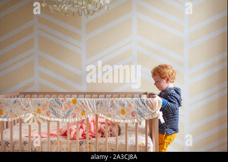 Il Toddler boy peeking in oltre il presepe rampa al neonato dormono in culla Foto Stock