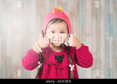 Incantevole piccola ragazza asiatica di indossare un abbigliamento informale gesticolando due pollici in su. Concetto di felicità e di soddisfazione Foto Stock