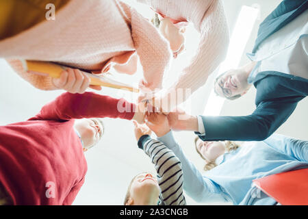 Studenti e insegnanti mani di impilamento come un team della scuola Foto Stock