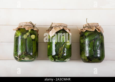 Tre grandi vasi con cetrioli fermentati giacciono su un bianco sullo sfondo di legno Foto Stock