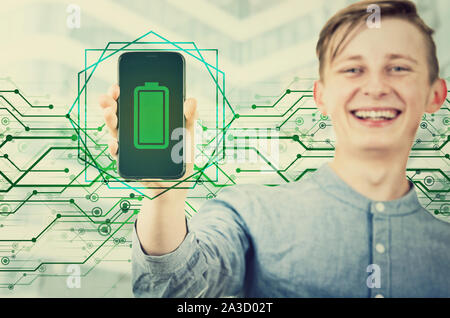 Felice ragazzo adolescente che mostra il suo smartphone con il pieno, verde la barra della batteria sullo schermo. Gioioso ragazzo adolescente presentando una nuova potente dispositivo. Tech Foto Stock