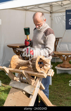 L'uomo la dimostrazione di artigianato in legno a Surrey Hills la fiera del legno, UK. Carving artigianali su misura di un tavolo di legno a mano. Foto Stock