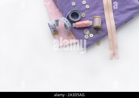 Accessori per il cucito e tessuti su uno sfondo bianco. Tessuto, fili di cucitura, aghi, pulsanti, zipper e la cucitura di centimetro. top view, flatlay Foto Stock