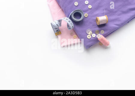 Accessori per il cucito e tessuti su uno sfondo bianco. Tessuto, fili di cucitura, ago, pulsanti e la cucitura di centimetro. top view, flatlay Foto Stock