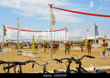 I giovani uomini a giocare a beach volley sulla spiaggia sabbiosa di Lido di Camaiore in una posizione soleggiata a metà agosto giornata con le biciclette parcheggiate, Versilia, Toscana, Italia Foto Stock