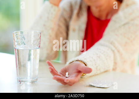 Donna che mantiene pillole con un bicchiere di acqua Foto Stock