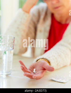 Donna che mantiene pillole con un bicchiere di acqua Foto Stock